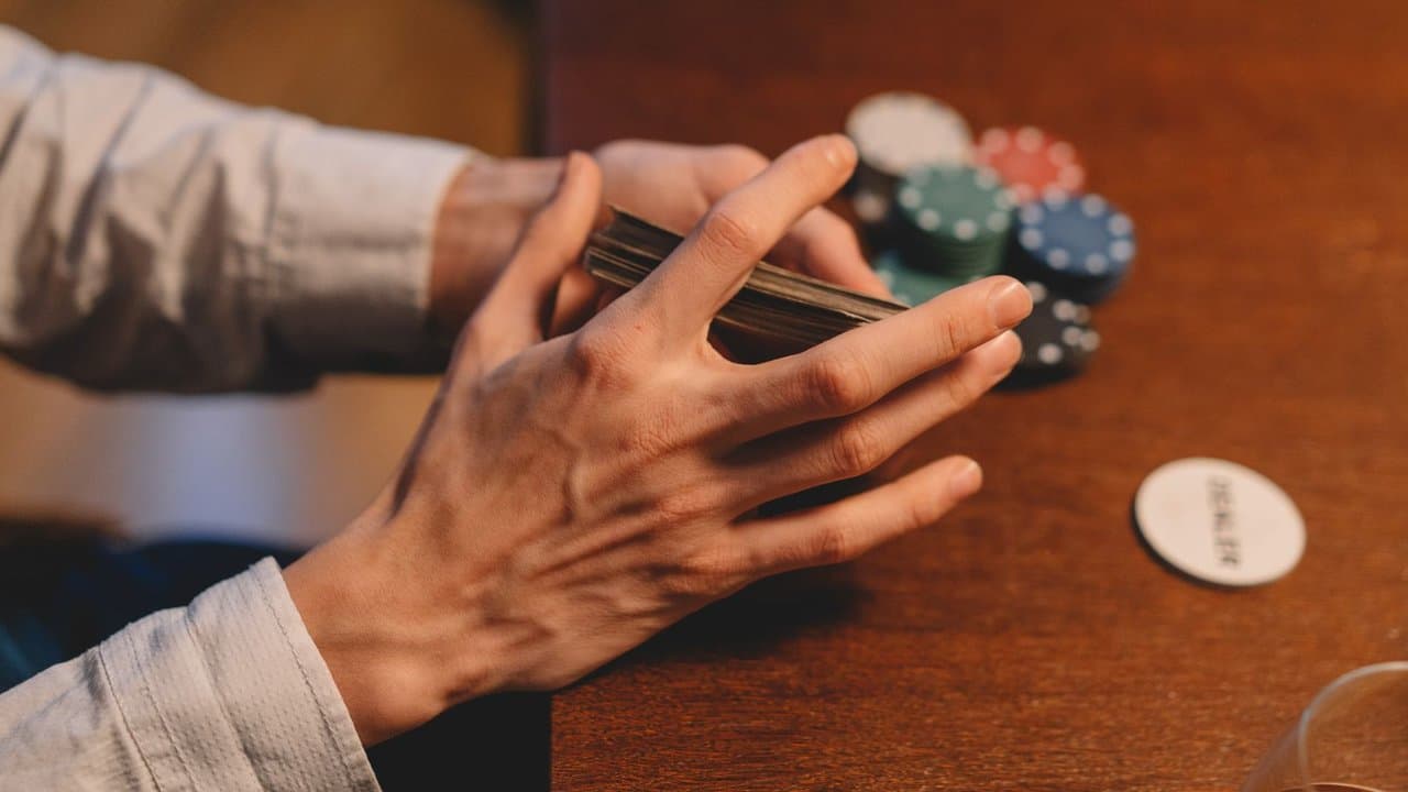 Hands holding playing cards and chips on a wooden gaming table